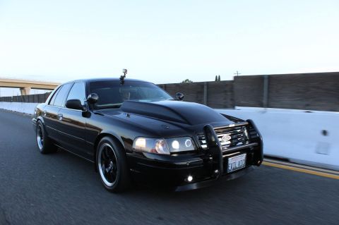 2003 Ford Crown Victoria - Photo of a black Crown Victoria police-style sedan with a push bar moving on a highway.