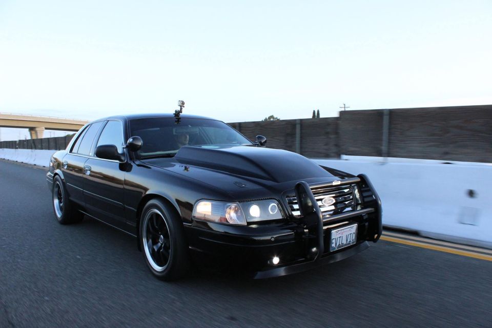Black Crown Victoria police interceptor with push bar driving on a roadway