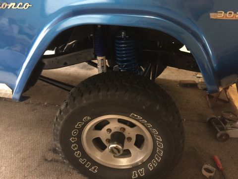1974 Ford Bronco - Close-up view of the front driver's side wheel well of a blue Ford Bronco, showing a large tire with white lettering and a blue shock absor…
