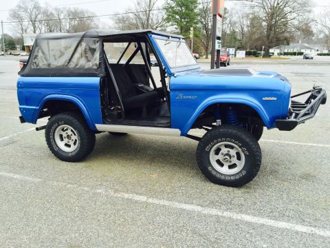 1974 Ford Bronco - A lifted, bright blue 1974 Ford Bronco with a black soft top and roll cage is parked on asphalt. Modifications include a custom front bumpe…