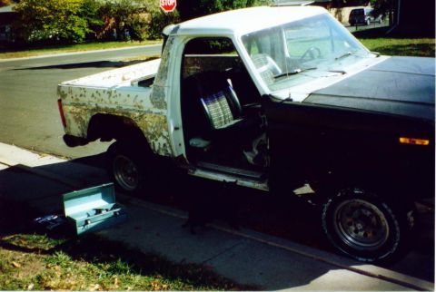 1981 Ford Bronco - Pickup truck with open doors and worn paint on the bed, parked on a street.