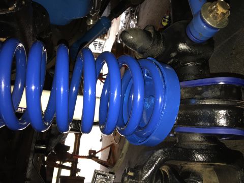 1974 Ford Bronco - A close-up view of a bright blue coil spring and suspension components on a vehicle. Black painted metal parts and blue polyurethane bushin…