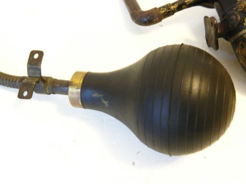 1915 Ford Model T - A close-up view of a black rubber bulb horn with a metal fitting and a ribbed texture, attached to a flexible metal hose. The horn is conne…