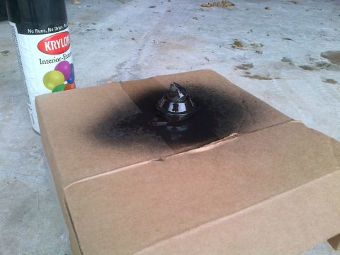 1915 Ford Model T - A can of Krylon spray paint sits next to a piece of cardboard with a small, dark object on it that has been spray painted black.