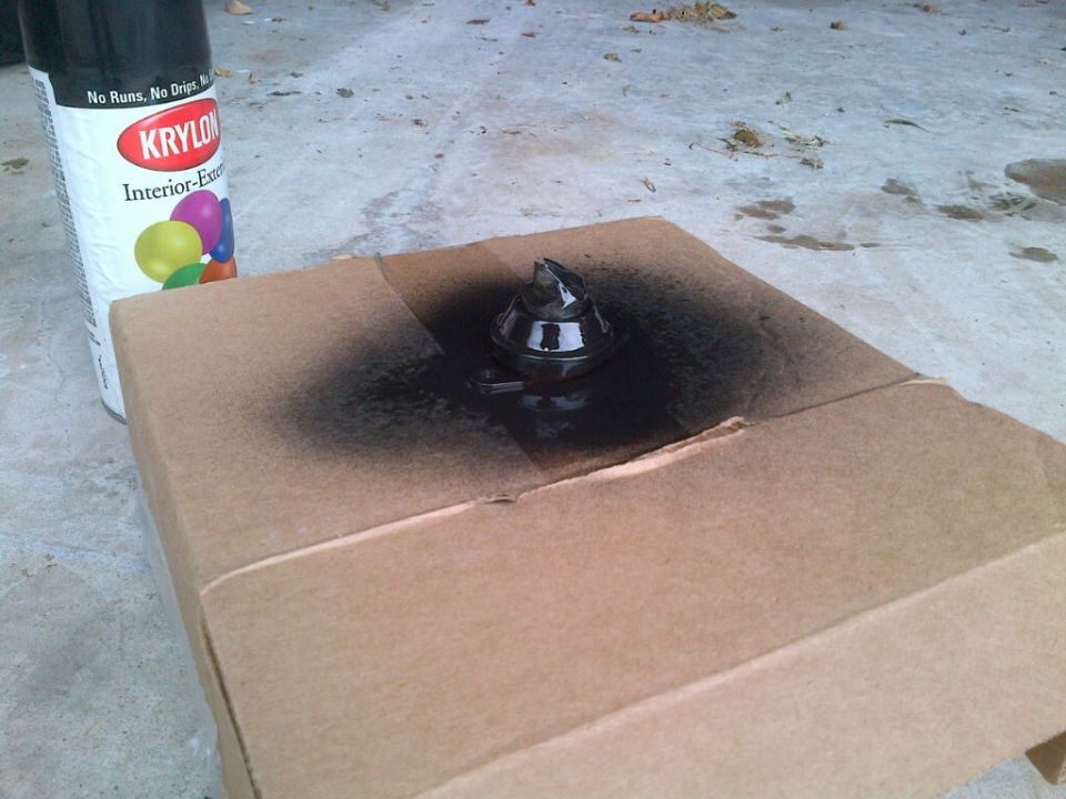Krylon spray paint can next to cardboard with a black painted object.