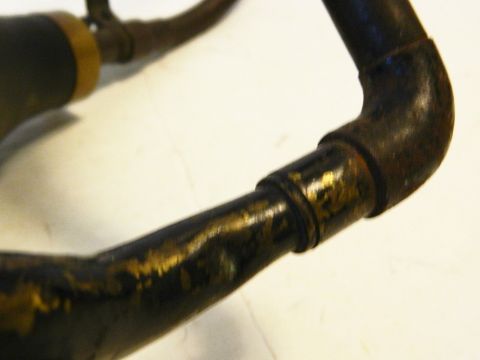 1915 Ford Model T - A close-up view of a dark, curved metal pipe with visible brass or gold accents and some rust. The pipe appears to be part of an older mech…