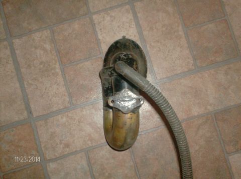 1915 Ford Model T - A close-up, overhead view of an old, brass and black metal part attached to a grey, ribbed hose, resting on a tiled floor. The part appears…