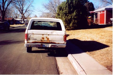 1981 Ford Bronco - The rear of a white Ford Bronco shows significant rust damage around the tailgate and bumper.