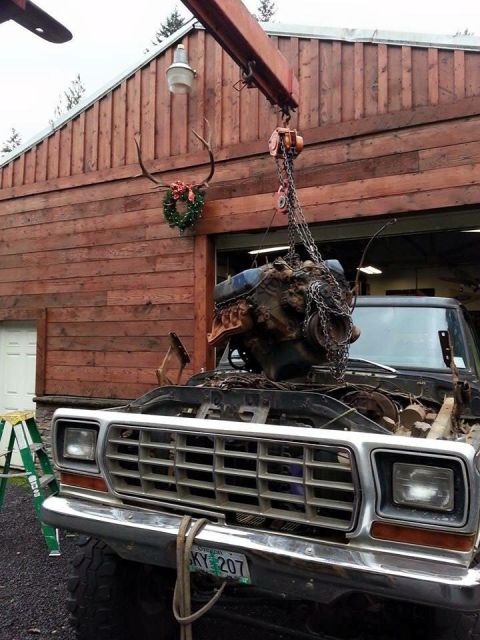 1979 Ford Bronco - An engine is being removed from a truck using an engine hoist in front of a wooden building.