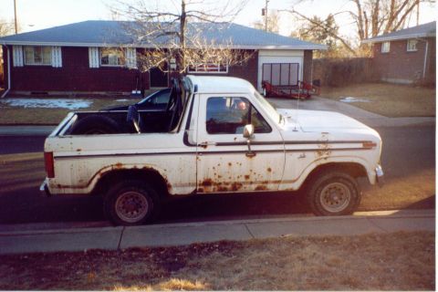1981 Ford Bronco - This heavily rusted white Ford Bronco is parked on the side of a residential street.