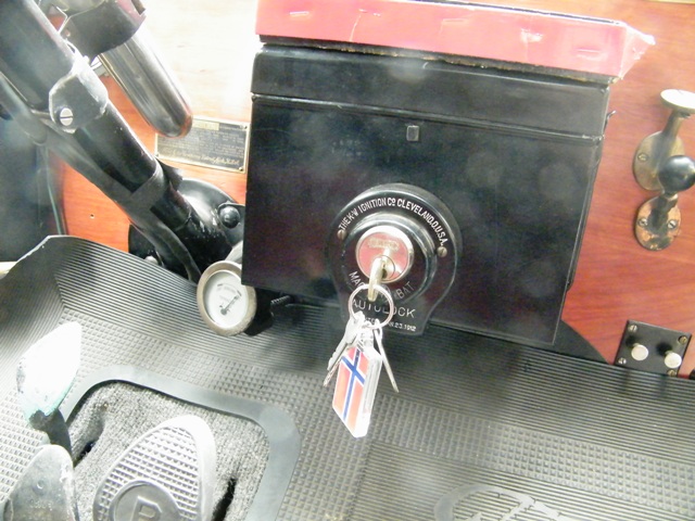 Interior of a vintage car showing an ignition switch with keys and a small gauge.