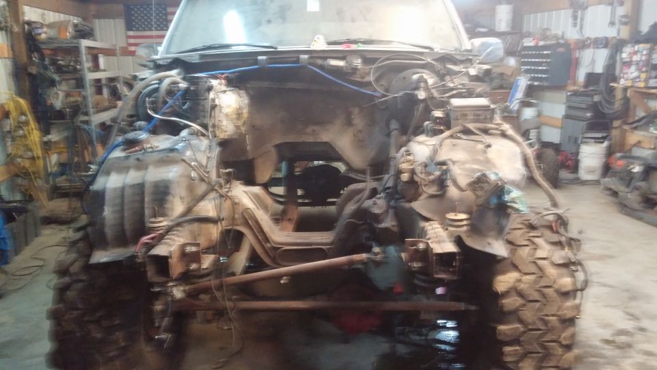 Front view of a disassembled 1995 Ford Bronco in a garage, showing the engine bay and chassis.