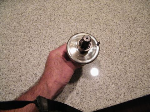 1909 Ford Model T - A hand holds a shiny metal automotive part with a shaft extending from the center. The part appears to be a pulley or a similar component,…