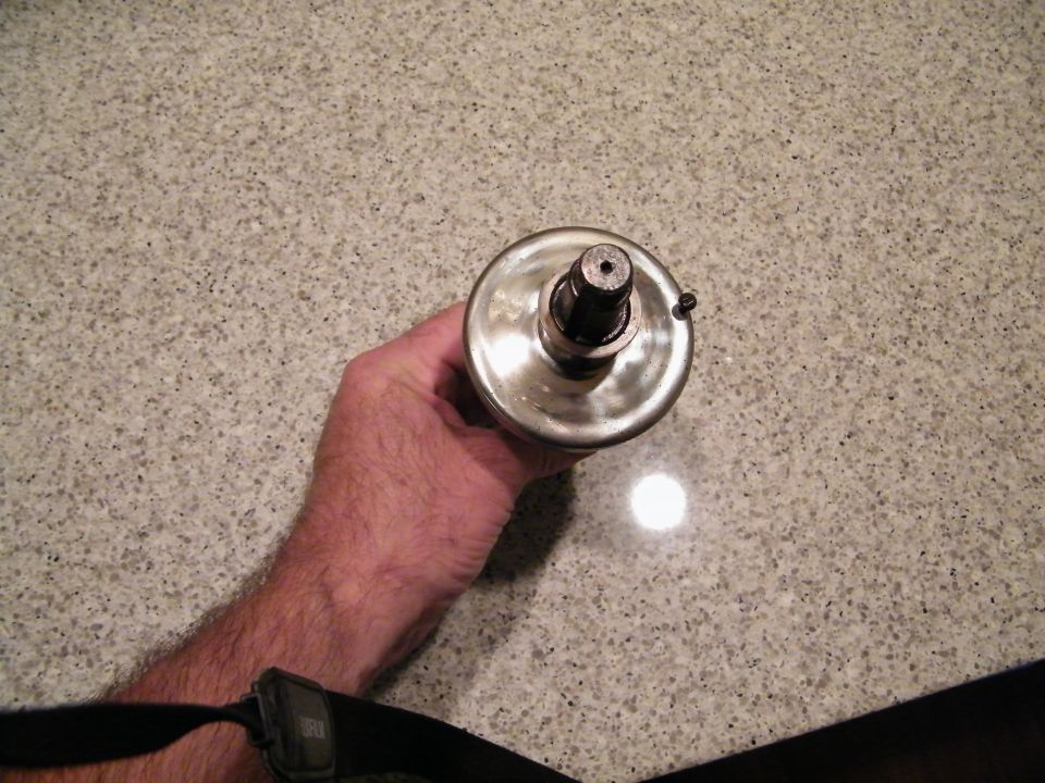 Shiny metal automotive part with a central shaft held by a hand.