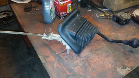 1995 Ford Bronco - A black rubber shifter boot and lever assembly with a black knob is resting on a rusty metal workbench. A Motorcraft oil filter box and a b…