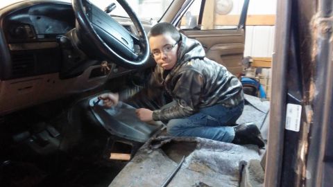 1995 Ford Bronco - A young person wearing glasses and a camouflage jacket kneels inside a vehicle, working on the floor near the dashboard and steering wheel.…