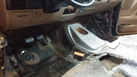 1995 Ford Bronco - The interior of a vehicle is shown with the floor mats removed, revealing the bare metal floor and the pedals. The dashboard and steering w…
