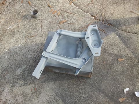 1976 Ford Ranchero - A gray painted metal hinge assembly with a coil spring is laid out on a concrete surface. The hinge appears to be a component for a vehicle…