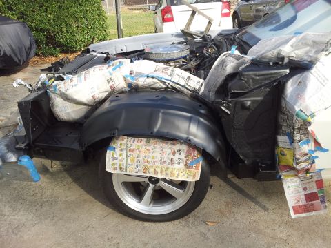 1976 Ford Ranchero - A partially disassembled vehicle, likely a Ford Ranchero, is covered in newspaper and blue tape. The front fender and wheel well are visibl…