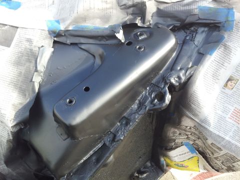 1976 Ford Ranchero - A close-up view of a black painted vehicle part, possibly a suspension component, resting on newspapers. The part has several bolt holes an…