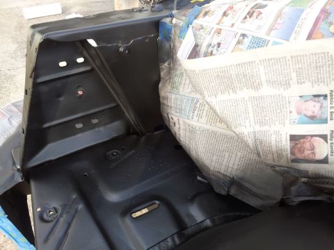 1976 Ford Ranchero - A black painted metal automotive part, possibly from the engine bay, is shown with newspaper used as protective covering. The newspaper con…