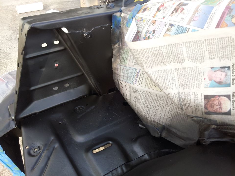 Black painted car part with newspaper covering, showing obituaries.