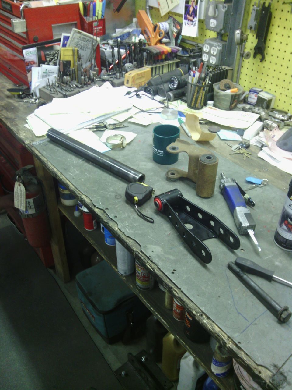Workbench with tools, parts, and papers. Includes a metal rod and suspension component.