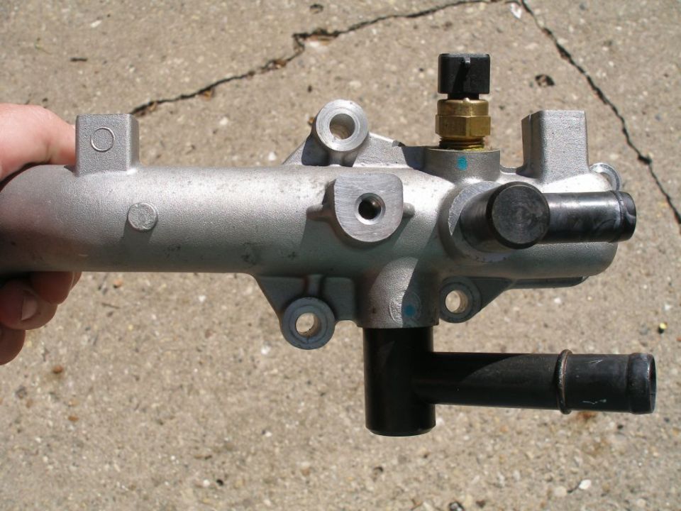 Silver metal automotive part with brass fitting and black cap, held in hand.