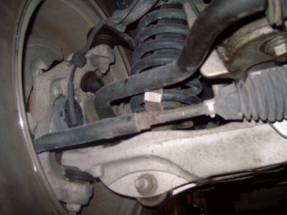 Close-up of front car suspension components: steering rack, sway bar, coil spring, control arm.