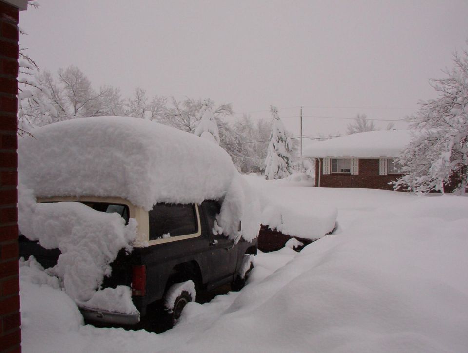 SUV buried in snow next to a house during a blizzard