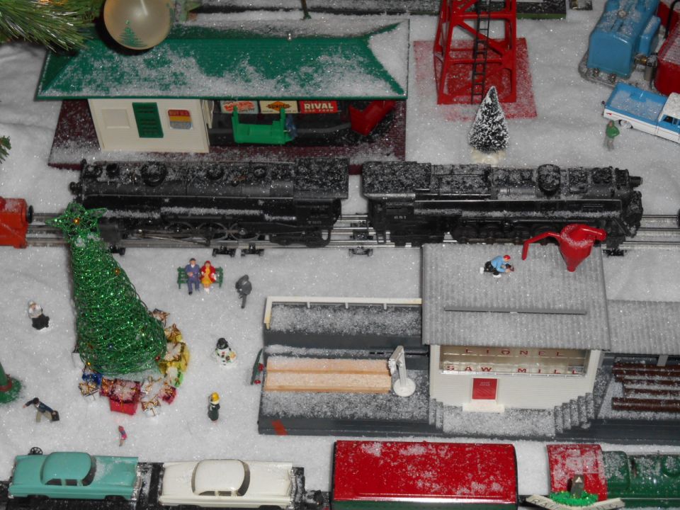 Miniature Christmas village scene with model trains, buildings, and tiny figures.
