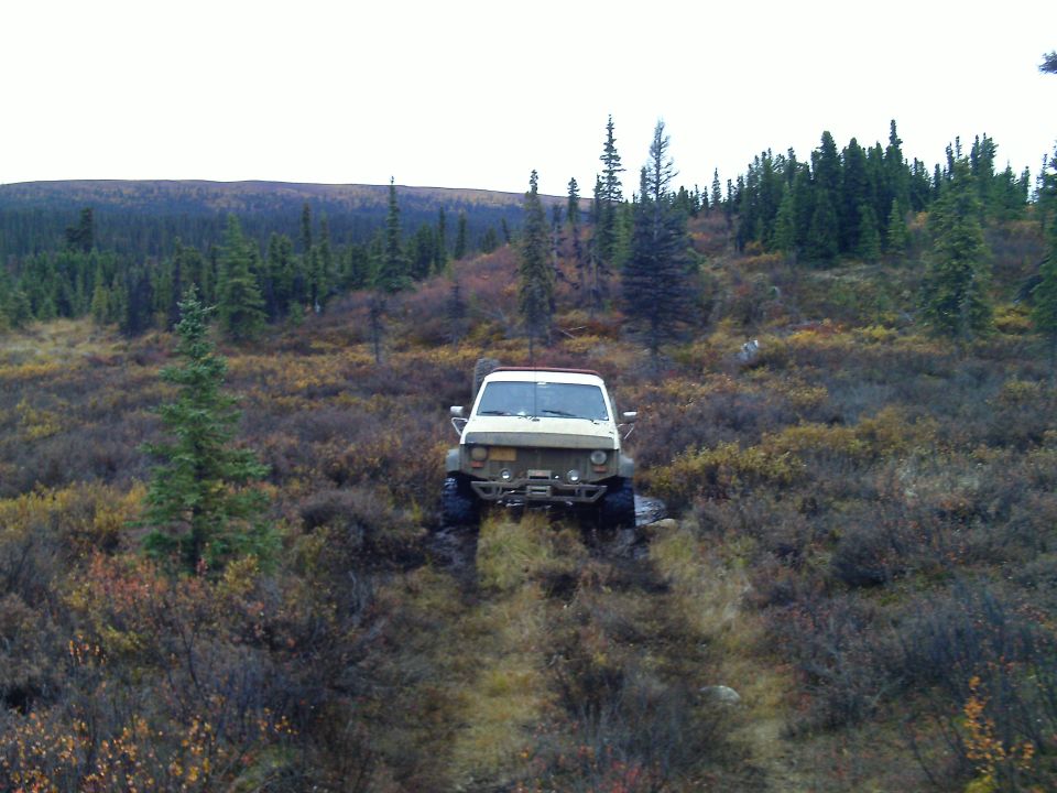 1990 Ford F-250 "Beast2" driving off-road in a wooded area with autumn foliage.