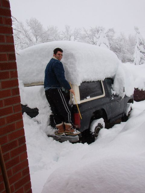 1981 Ford Bronco - A man attempts to clear a thick blanket of snow from a 1981 Ford Bronco during a winter storm.