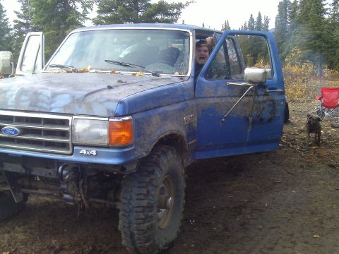 1990 Ford F-250 - A muddy 1990 Ford F-250 truck sits in a wooded area with its driver's door ajar.