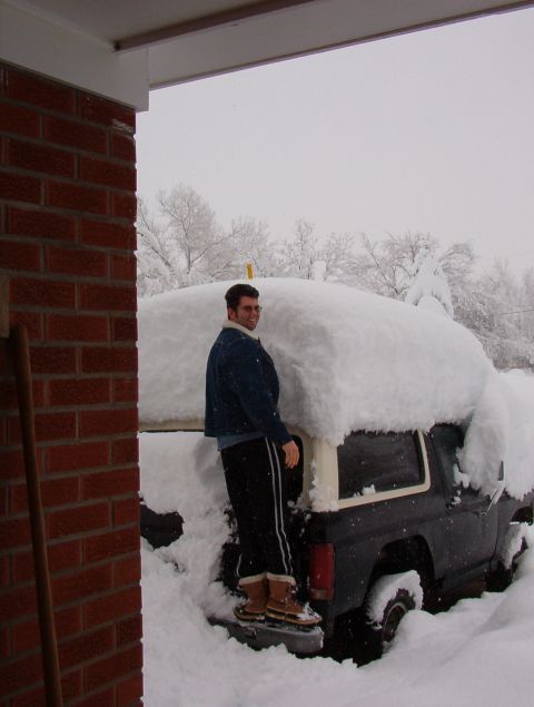 1981 Ford Bronco - A man stands on a snow-covered SUV, possibly a Ford Bronco, during a winter storm.