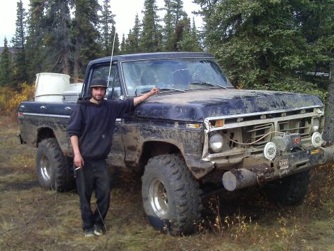 1990 Ford F-250 - A man poses next to a muddy, dark blue pickup truck in a wooded area.