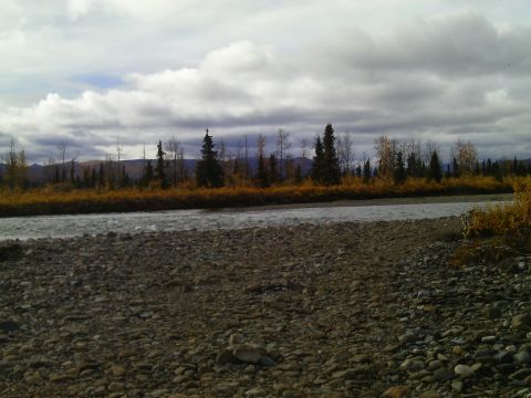 1990 Ford F-250 - A wide river flows through a rocky landscape, bordered by trees in autumn colors under a cloudy sky.