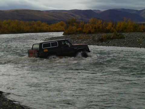 1990 Ford F-250 - SUV navigates a river during autumn, with wooded hills and mountains visible.