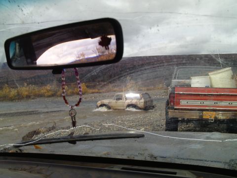 1990 Ford F-250 - Two trucks navigate a shallow river, one a tan Ford Bronco and the other a red Ford pickup.