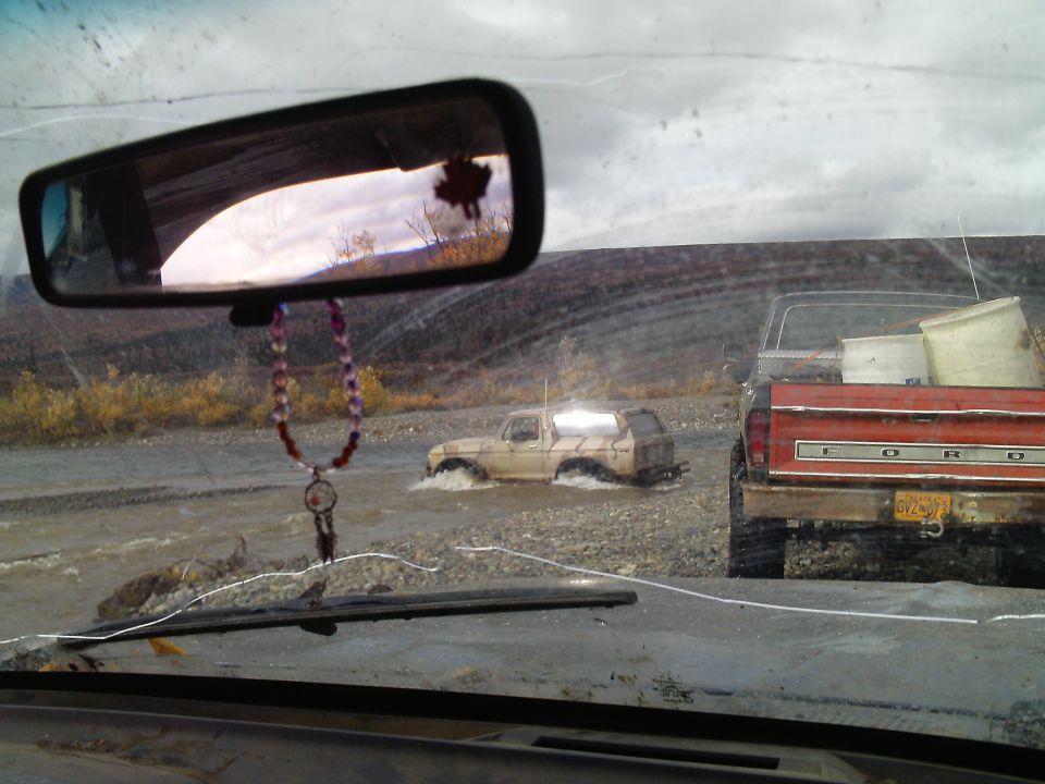 Tan Ford Bronco driving through water, red Ford pickup truck in foreground