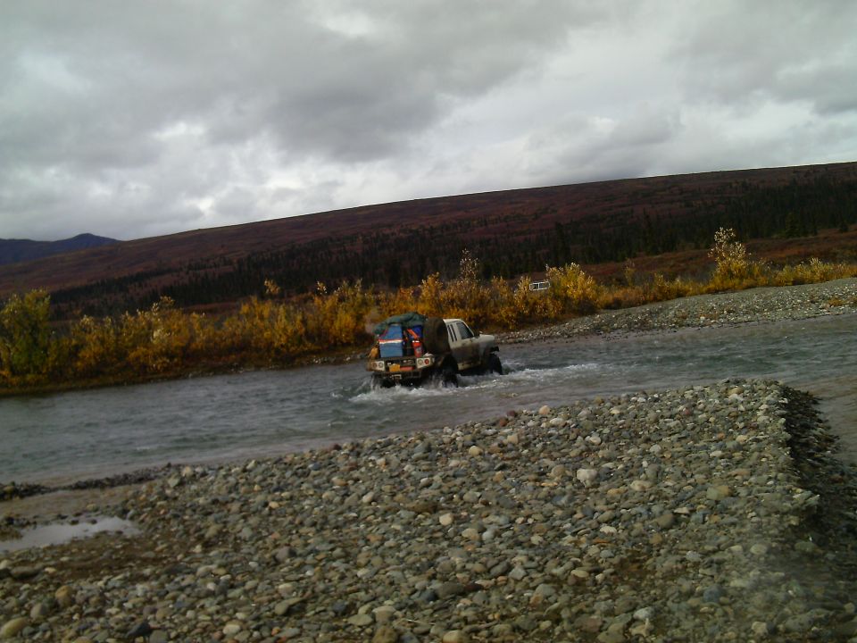 1990 Ford F-250 crossing a river, loaded with gear on the bed