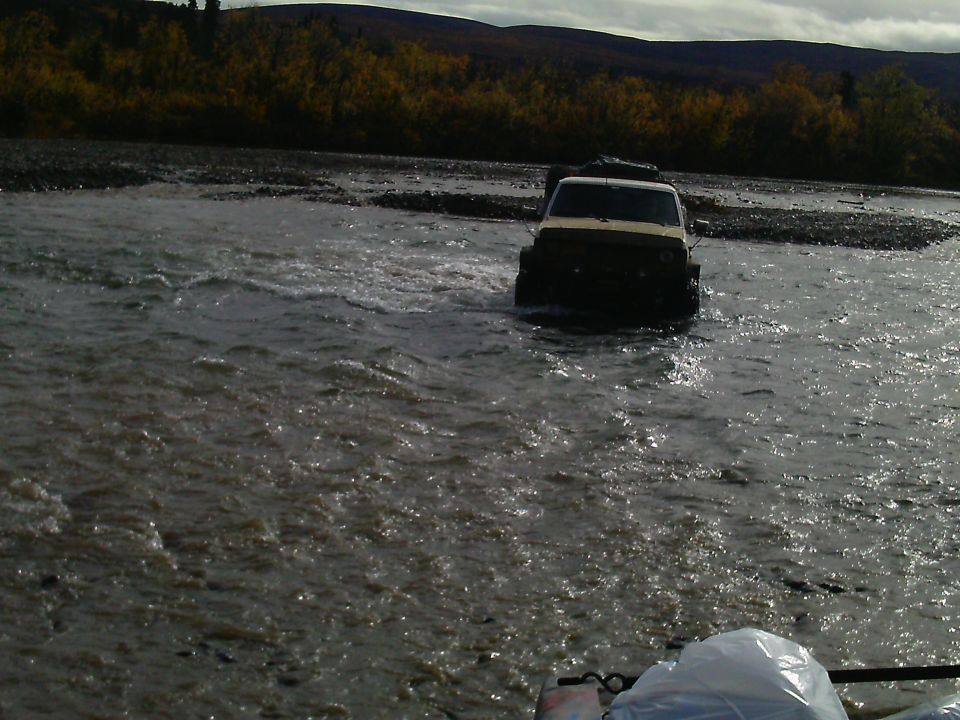White SUV fording a river with trees in background