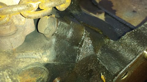 1995 Ford Bronco - Close-up view of an engine block, showing a chain and bolt, with visible oil residue.