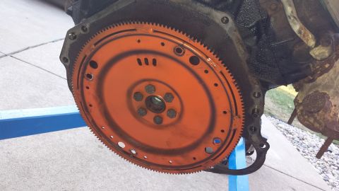 1995 Ford Bronco - Close-up of an engine block and its orange flywheel, mounted on an engine stand.