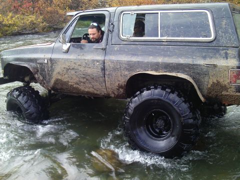 1990 Ford F-250 - This lifted K5 Blazer is navigating through a stream, kicking up water as it goes.