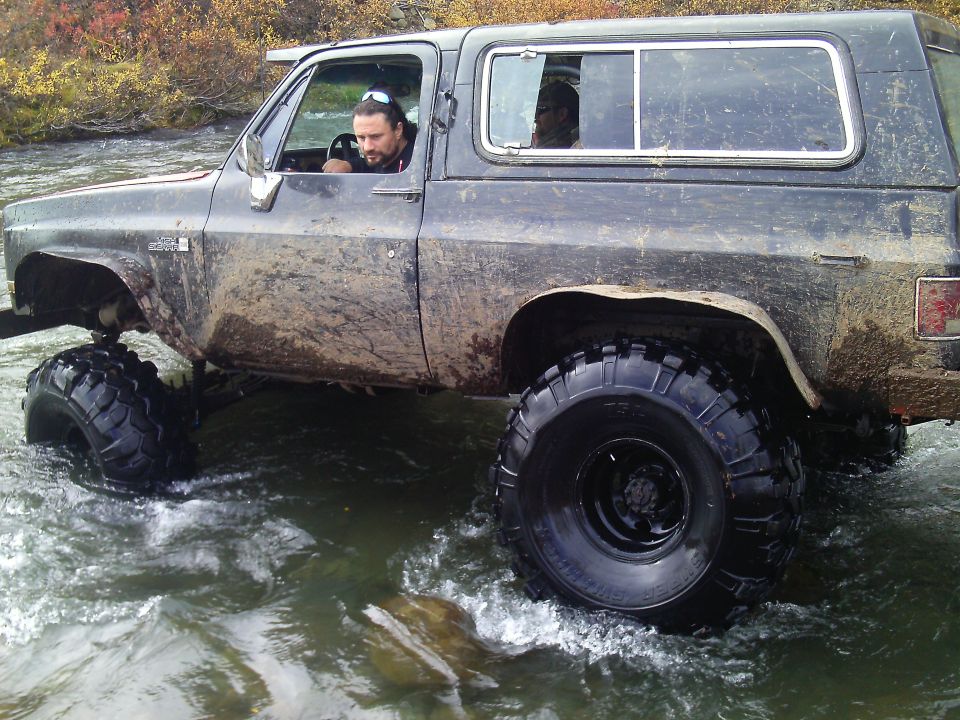 Lifted K5 Blazer driving through a shallow river with a man driving