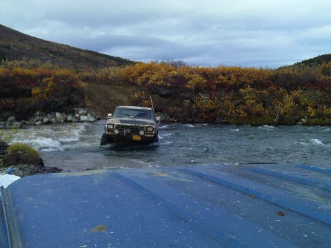 1990 Ford F-250 - A Ford F-Series truck navigates a shallow river during autumn, with another vehicle's hood visible in the foreground.