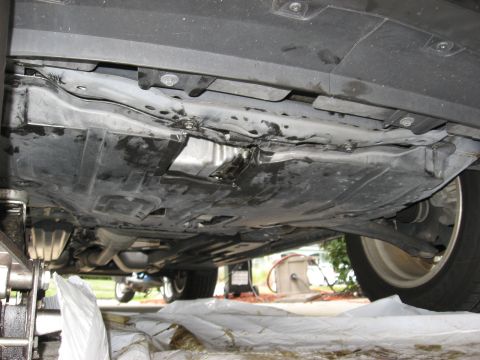 1994 Ford Bronco - The underside of a vehicle is shown, revealing the undercarriage and plastic shielding, with a jack visible on the left.
