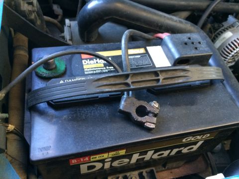 1990 Ford Bronco - A close-up view of a car battery and its disconnected terminal clamp.