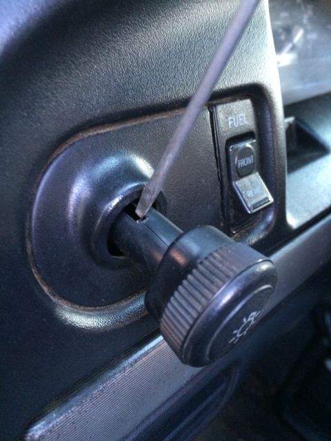 1990 Ford Bronco - A screwdriver is used to turn the headlight switch knob inside a vehicle's interior. Adjacent buttons are labeled FUEL and FRONT.